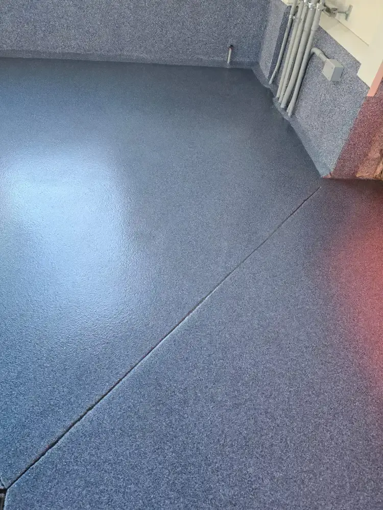 Glossy blue flake epoxy floor with a coated wall base in a car wash