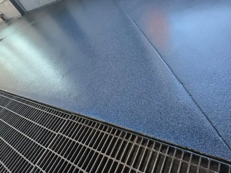 Blue flake epoxy floor meeting a steel drain grate in a car wash