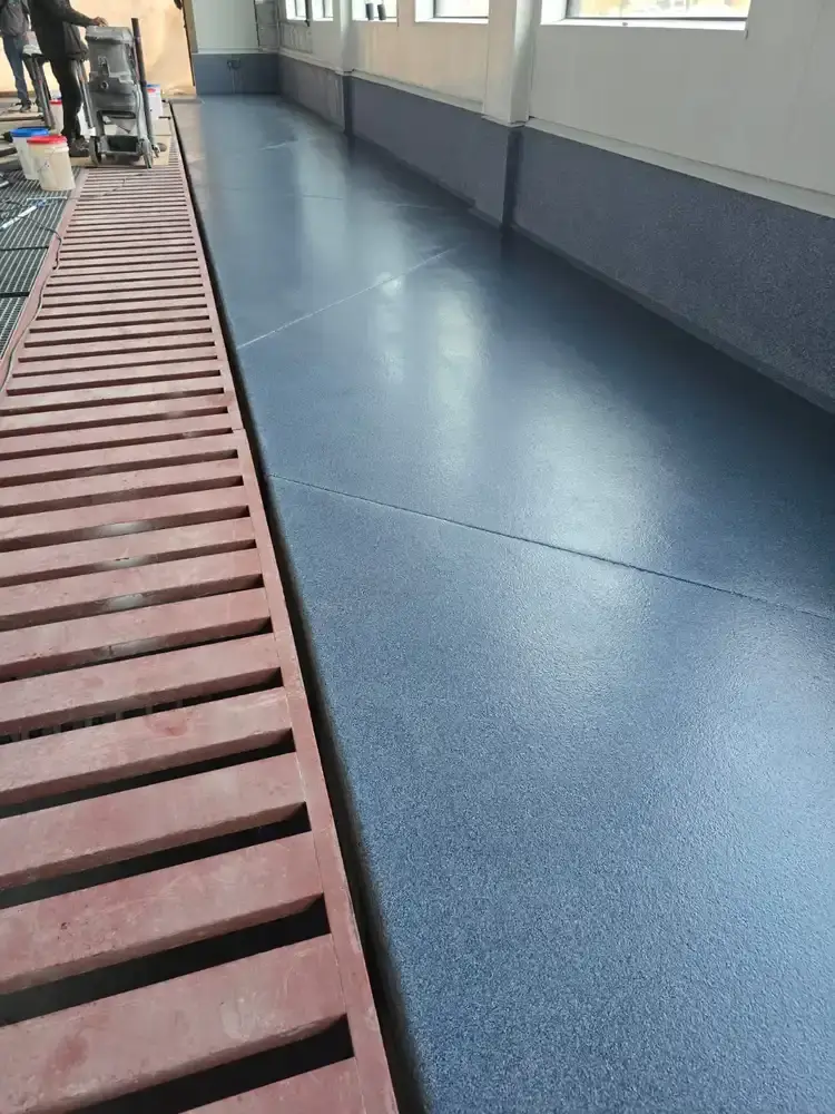 Blue flake epoxy floor beside a long trench drain in a car wash bay