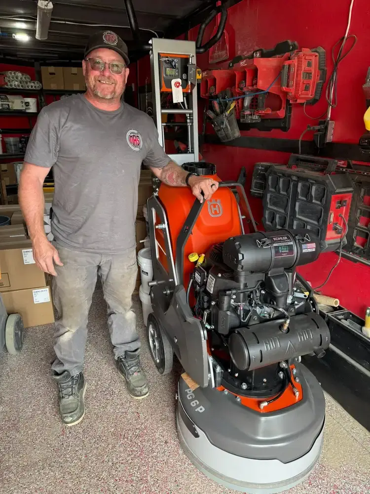 Mike Toupin standing beside a Husqvarna concrete grinder inside the company trailer