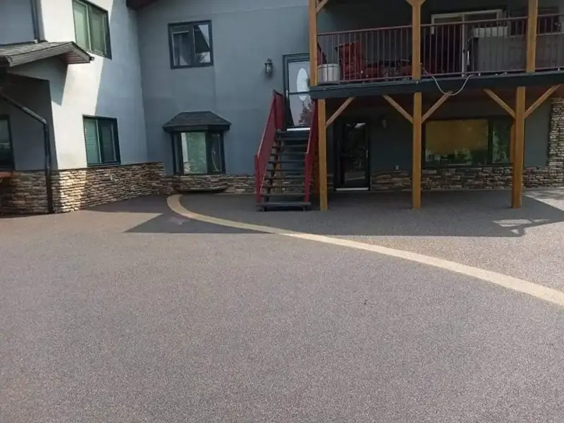 Curved rubber-paved driveway beside a house with a raised deck